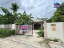 Photo of the front exterior of a house with a sign listing the property for sale.