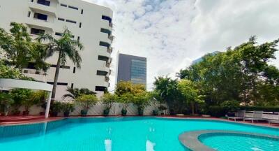 Outdoor swimming pool area with trees and nearby buildings