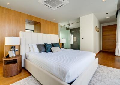 Modern bedroom with a large white bed, wooden accents, and an en-suite bathroom