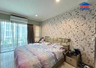 Bedroom with a large bed, floral wall design, bedside tables, and large windows with curtains