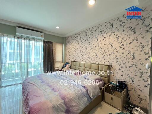 Bedroom with a large bed, floral wall design, bedside tables, and large windows with curtains