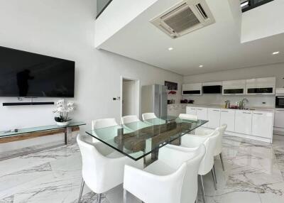 Modern kitchen and dining area with glass table, white chairs, TV, and appliances