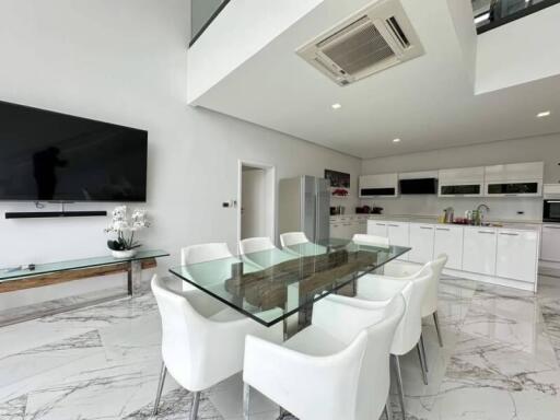 Modern kitchen and dining area with glass table, white chairs, TV, and appliances