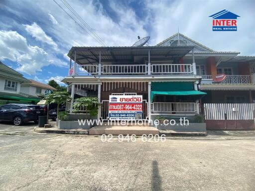 Exterior view of a two-story residential building with a signboard showing contact details for Inter Real Estate