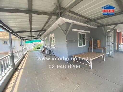 Photo of a covered outdoor area attached to a building with railings, windows, and a bed frame.