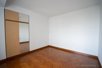 A minimalistic bedroom with wooden parquet flooring and wall-mounted storage