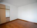 A minimalistic bedroom with wooden parquet flooring and wall-mounted storage