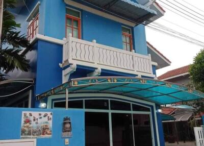 Front view of a blue two-story house with a balcony, canopy, and driveway