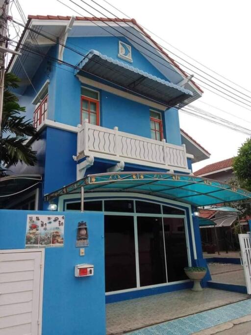 Front view of a blue two-story house with a balcony, canopy, and driveway