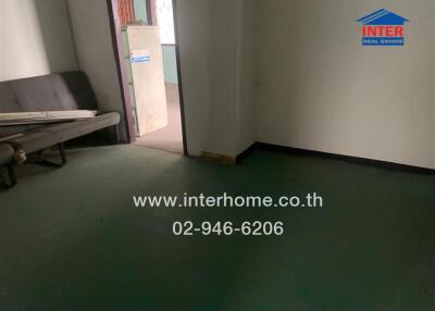 Partially furnished room with green carpet, sofa, and door leading to another area