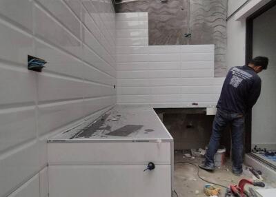 Modern kitchen under renovation with white wall tiles and a worker