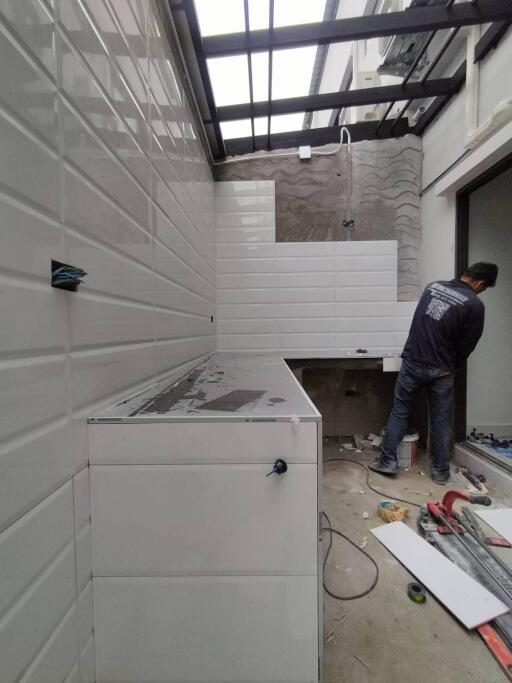 Modern kitchen under renovation with white wall tiles and a worker