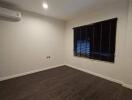 Empty bedroom with wooden floor, air conditioning, and window with blinds