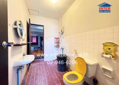 Bathroom with red tile floor, white tiled walls, yellow toilet seat, sink, and mirror