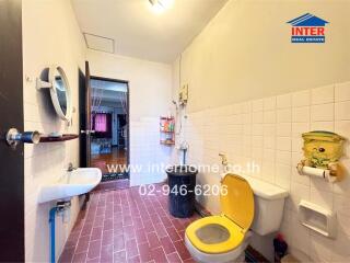 Bathroom with red tile floor, white tiled walls, yellow toilet seat, sink, and mirror