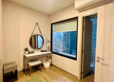 Bedroom with a green rug, mirror, small table, and window overlooking bathroom.