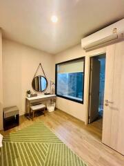 Bedroom with a green rug, mirror, small table, and window overlooking bathroom.