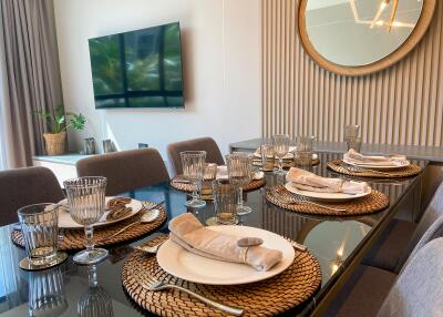 Elegant dining room with a glass table set for a meal, featuring modern décor and a large TV on the wall