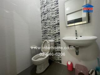 Modern bathroom with a tiled wall, a toilet, and a sink.