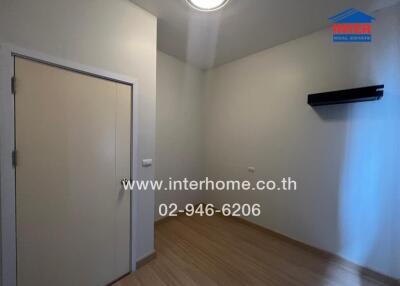 Empty bedroom with wooden floor and door, lit by ceiling light.