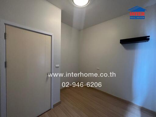 Empty bedroom with wooden floor and door, lit by ceiling light.