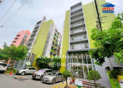 Facade of a multi-story residential building with parking area and trees