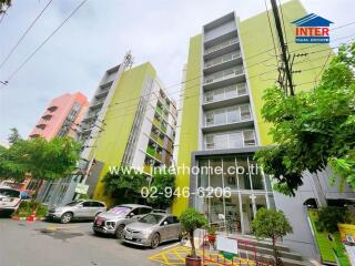 Facade of a multi-story residential building with parking area and trees