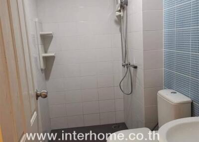 Modern bathroom with shower, toilet, and sink featuring tiled walls and floor.