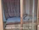 Bedroom with bed and curtains visible through a glass sliding door