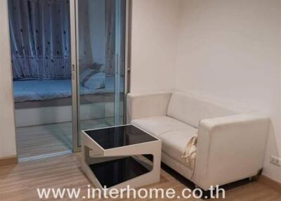 Living room with white sofa and small table, and view into the bedroom