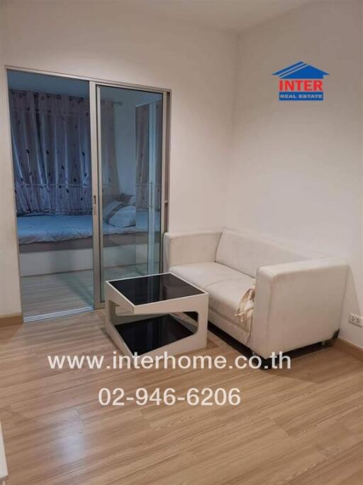 Living room with white sofa and small table, and view into the bedroom