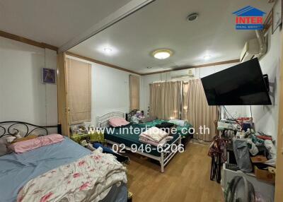 Bedroom with two beds, large television, window air conditioning, and various items.