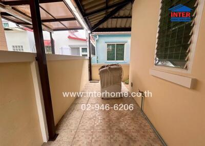 Covered outdoor corridor with tiled flooring, windows, and a utility area