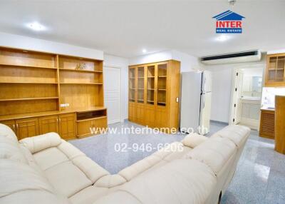 Spacious living room with built-in wooden shelves, white sofa, and adjacent kitchen area