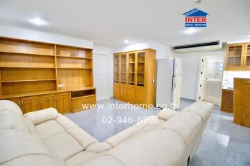 Spacious living room with built-in wooden shelves, white sofa, and adjacent kitchen area