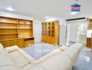 Spacious living room with built-in wooden shelves, white sofa, and adjacent kitchen area