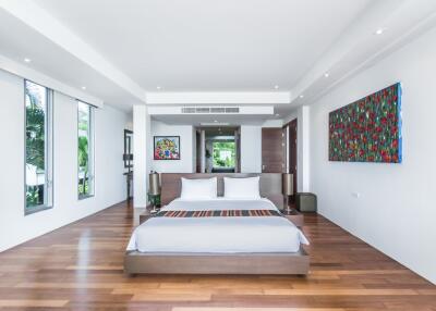 Spacious and modern bedroom with a large bed, wooden floors, colorful artwork, and ample natural light.