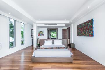 Spacious and modern bedroom with a large bed, wooden floors, colorful artwork, and ample natural light.