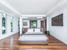 Spacious and modern bedroom with a large bed, wooden floors, colorful artwork, and ample natural light.