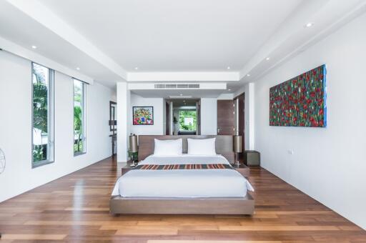 Spacious and modern bedroom with a large bed, wooden floors, colorful artwork, and ample natural light.