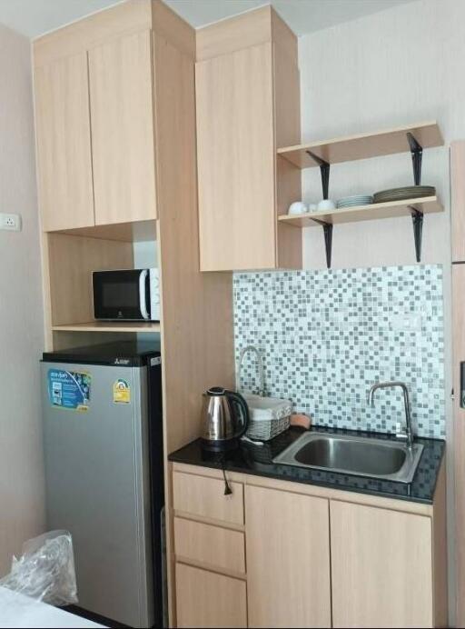 Compact kitchen with wooden cabinets, a small fridge, a microwave, and a sink