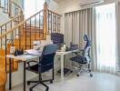 Home office setup under staircase with desk chairs, computer, and natural light