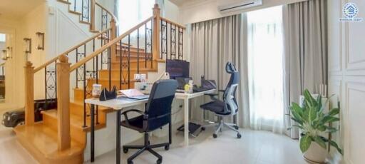 Home office setup under staircase with desk chairs, computer, and natural light