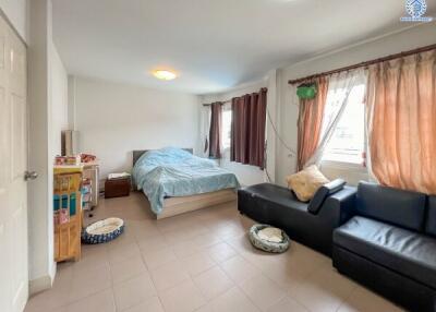 A bright bedroom with a bed, couch, windows, and various furniture.