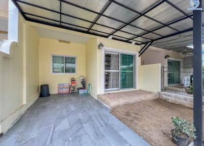 Covered outdoor area of a building with tiled flooring, sliding glass doors, and a small gated garden space.