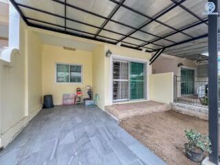 Covered outdoor area of a building with tiled flooring, sliding glass doors, and a small gated garden space.