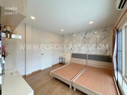 A modern bedroom with a double bed, marble accent wall, wooden flooring, and large windows.