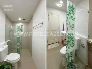 Modern bathroom with white and beige tiles, toilet, shower area with glass partition, and door