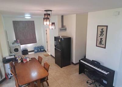 Dining area with a wooden table, chairs, washing machine, fridge, and piano