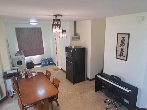 Dining area with a wooden table, chairs, washing machine, fridge, and piano